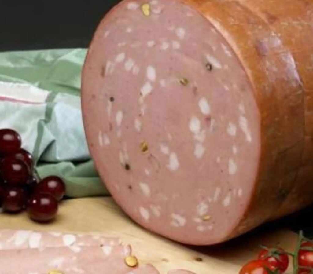 Pieza de mortadela cortada sobre tabla de madera con uvas y tomates