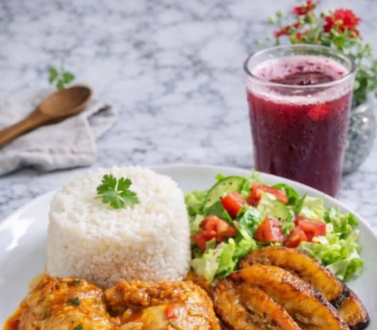 Plato de almuerzo con arroz, pollo guisado, tajadas y ensalada junto a un jugo