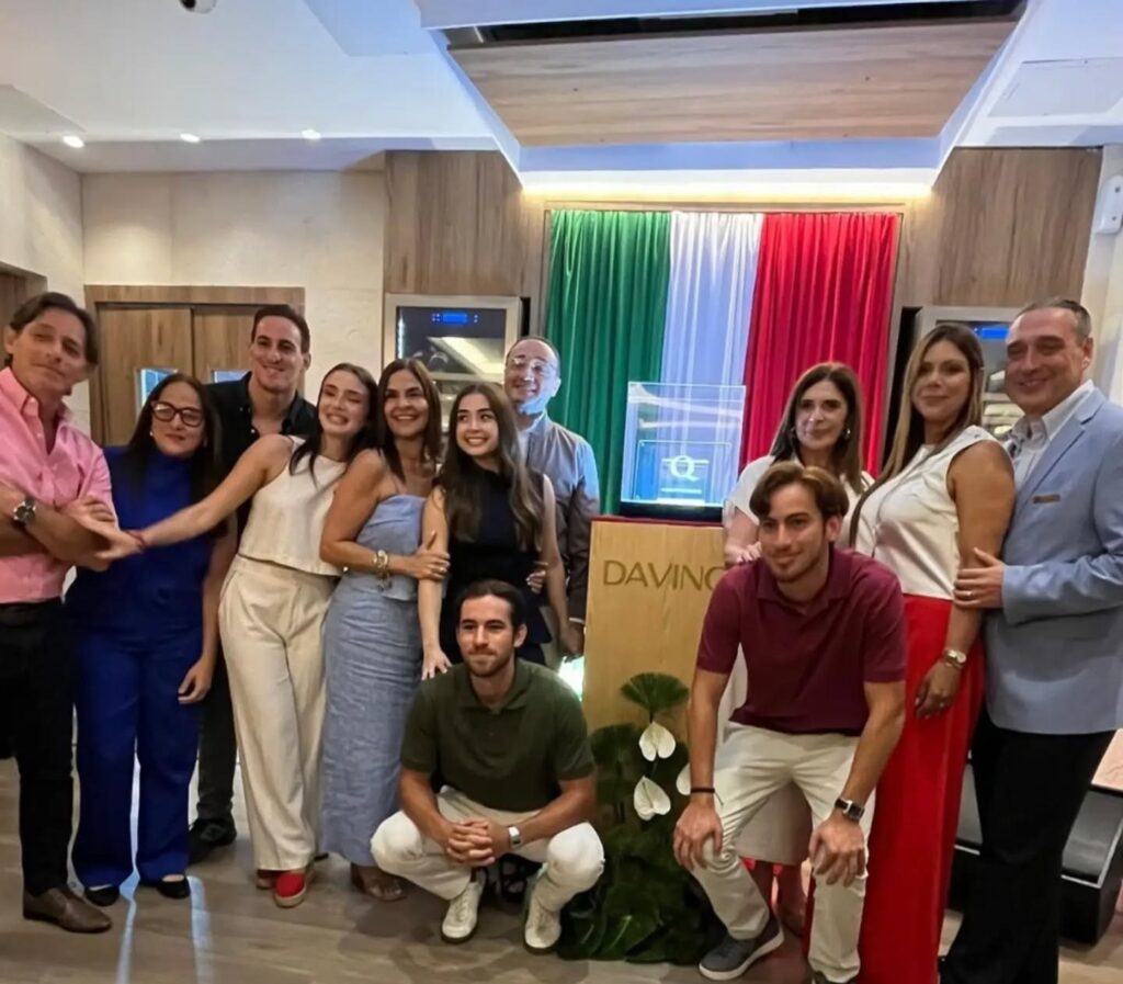 La familia Anaclerio posa frente a la bandera de Italia junto a la certificación Marchio Ospitalità Italiana