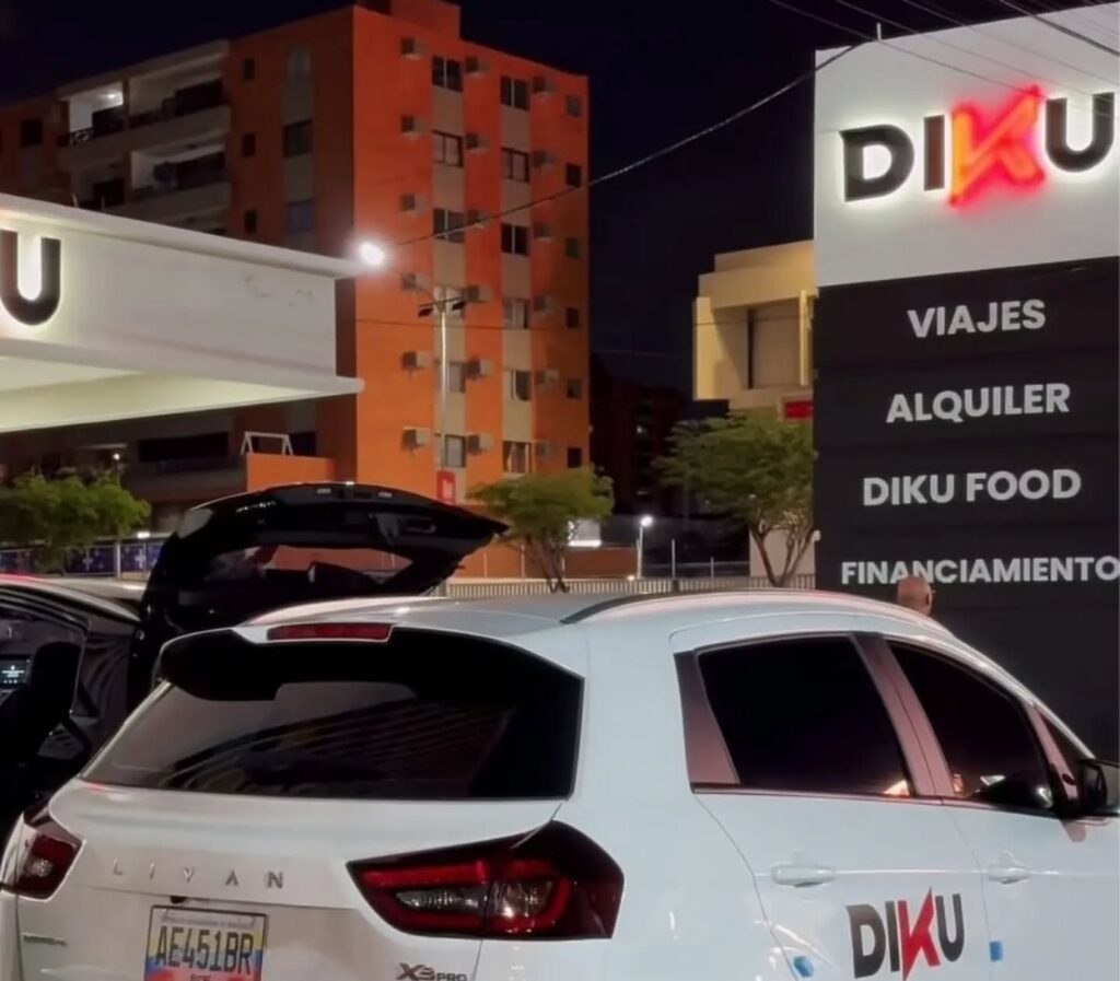 Vehículo blanco con el logo de Diku frente a su sede, con un cartel de viajes, alquiler y financiamiento